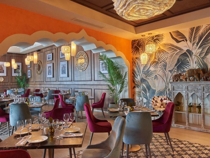 Elegant restaurant with colorful chairs, wood paneling, and botanical wall decor.