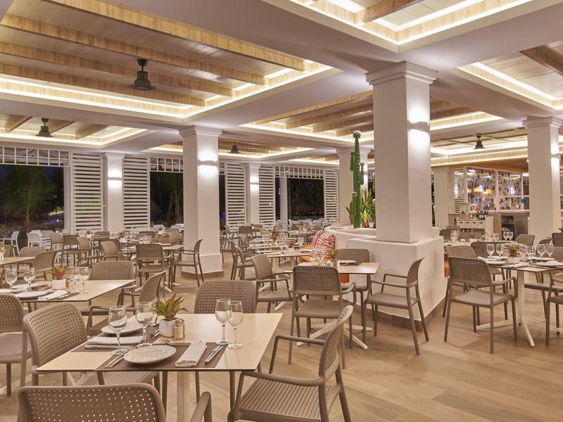 Modern, bright hotel restaurant with wooden ceiling and many set tables.