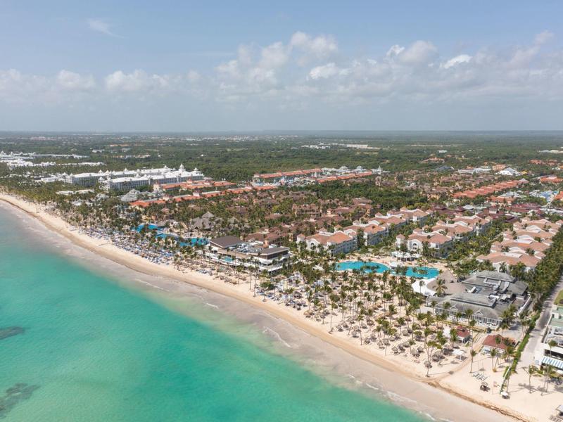 Aerial view of a resort on a white sandy beach with turquoise sea and blue pools.