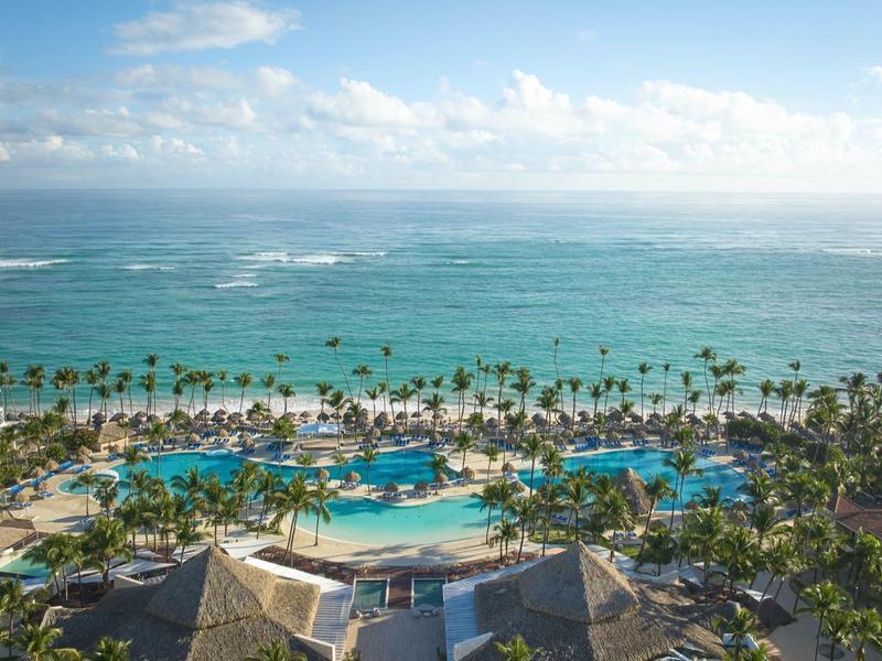 View of a tropical resort with pool, palm trees, and ocean under a blue sky.