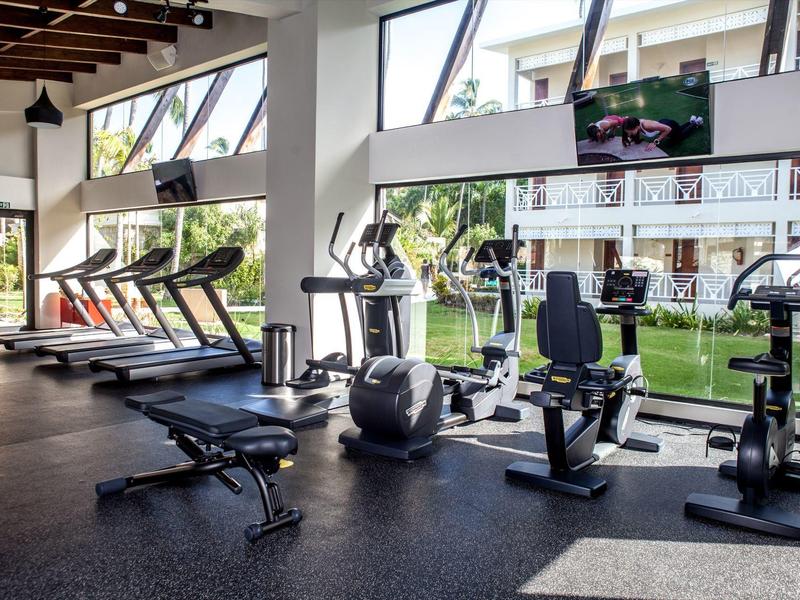 Gimnasio luminoso con varias máquinas de entrenamiento y grandes ventanas con vistas al jardín.