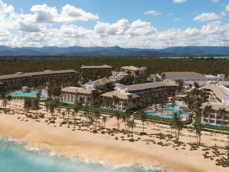 Resort di lusso sulla spiaggia con piscine, palme e vista mare sotto un cielo parzialmente nuvoloso.