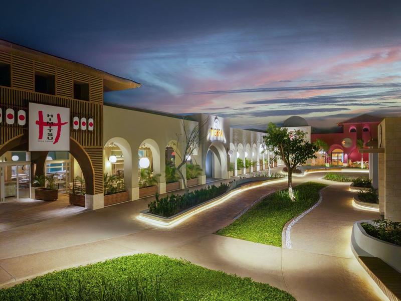 Vista di un complesso alberghiero moderno illuminato con sentieri e aree verdi al tramonto.