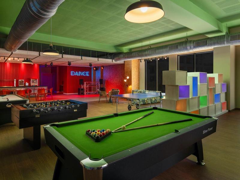 Sala ricreativa moderna con tavolo da biliardo, calcetto e pareti divisorie colorate con illuminazione soffusa.