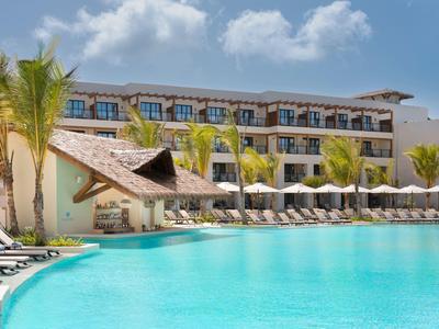 Moderner Hotelkomplex mit großem Pool und Liegestühlen bei sonnigem Wetter.