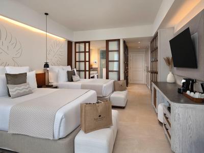 Světý hotelový pokoj se dvěma postelemi, moderním nábytkem a televizí na zdi.