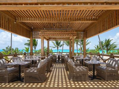 Otevřená lounge s dřevěnou střechou a pohodlnými pohovkami s výhledem na tropickou krajinu a moře.