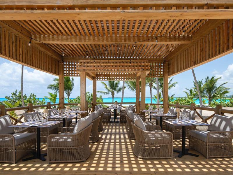 Otevřená lounge s dřevěnou střechou a pohodlnými pohovkami s výhledem na tropickou krajinu a moře.