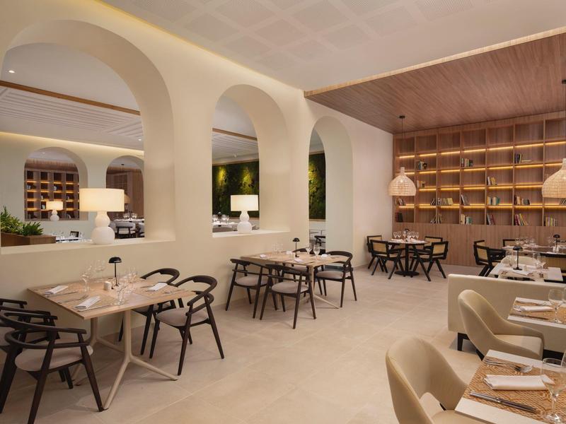 Moderní restaurace se světlými zdmi, obloukovými otvory a stylovým dřevěným nábytkem.