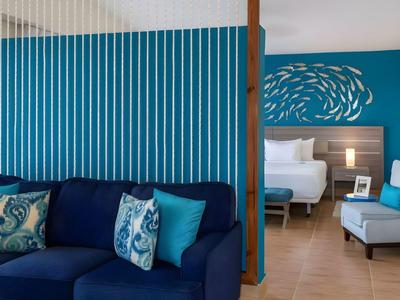 Moderne hotelkamer met blauwe bank, stoel en een bed op de achtergrond.