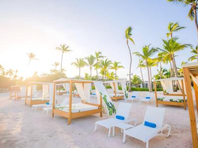Sonnige Poolarea mit Liegestühlen und Pavillons, umgeben von Palmen.