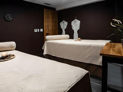 Gästeraum mit zwei behandelten Massageliegen und dunklen Wänden.