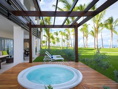 Bubbelbad op houten terras met uitzicht op tuin en palmbomen aan zee.