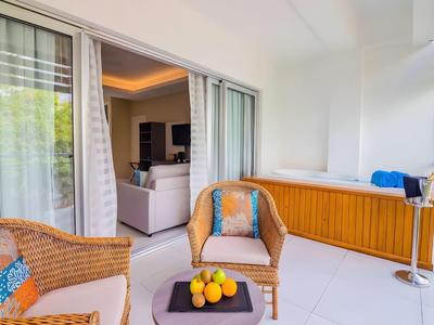 Balkon met rotan stoelen, tafel en uitzicht op een lounge met bank in een hotelkamer.
