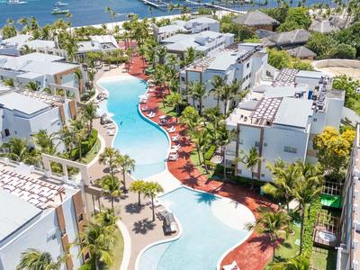 Vista aerea di un resort con piscina moderna, edifici bianchi e palme.
