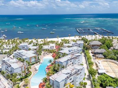 Una località costiera con piscine, edifici bianchi e spiaggia di sabbia vicino a un mare blu sotto un cielo nuvoloso.