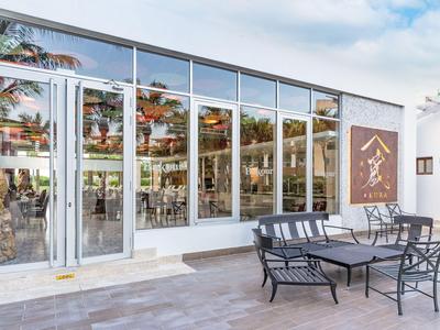 Giardino dell'hotel moderno con facciata in vetro, sedie e tavoli sulla terrazza sotto un cielo azzurro.