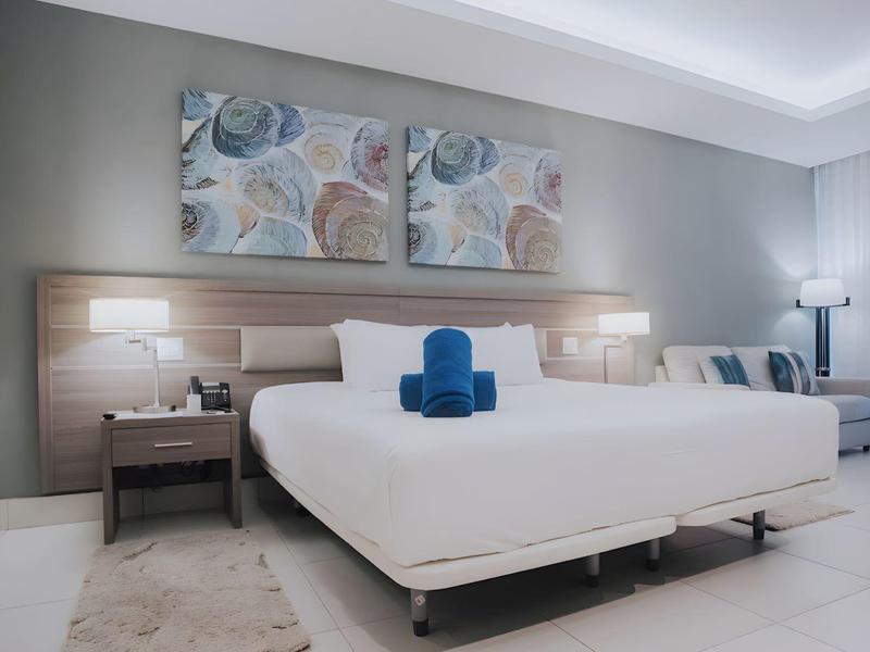 Modern hotelkamer met groot tweepersoonsbed, nachtkastjes en rustige kleuren.