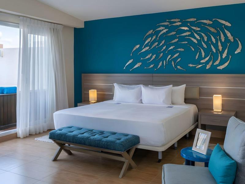 Moderne hotelkamer met tweepersoonsbed, blauwe muur en bankje bij het raam.