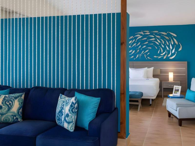 Moderne hotelkamer met blauwe bank, stoel en een bed op de achtergrond.