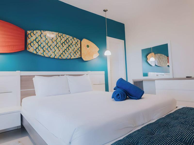 Modern hotelkamer met groot bed, vis aan de muur en blauwe accenten.