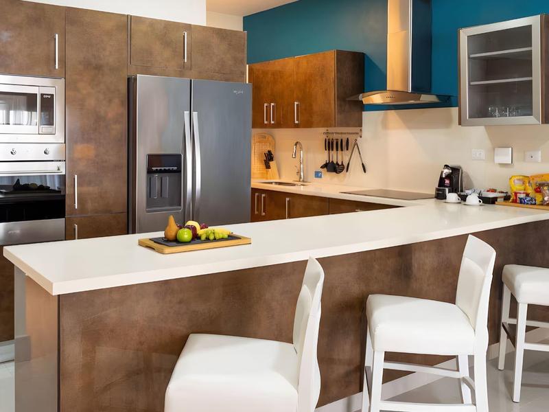 Moderne keukenhoek met roestvrijstalen apparaten, bar met witte stoelen en warme houten fronten.