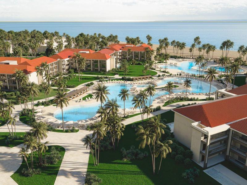 Een tropisch resort met gebouwen met rood dak rondom grote, kronkelige zwembaden en palmbomen.