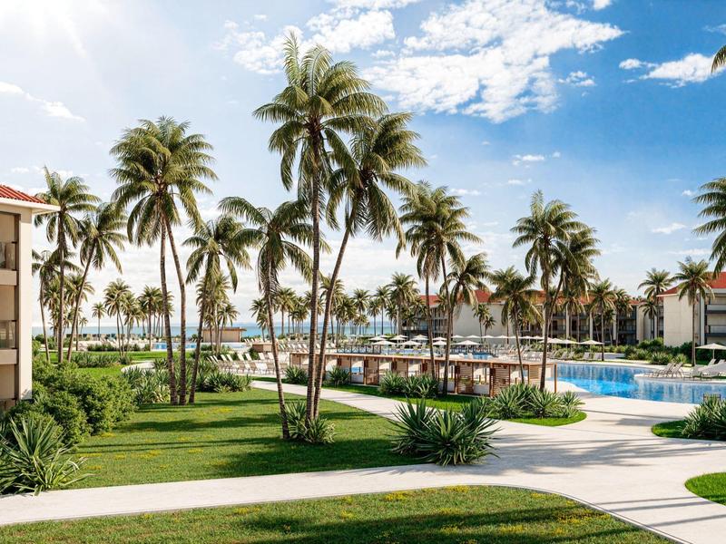 Zonnig resort met palmbomen, zwembad en pad bij hotelgebouwen aan zee.