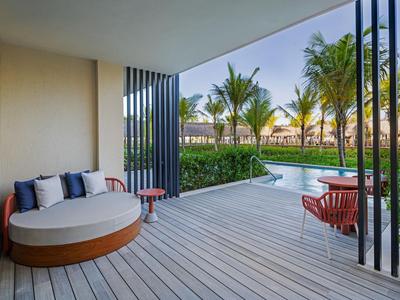 Terrasse mit modernem runden Sofa und Blick auf Pool und Palmen in einem Hotel.