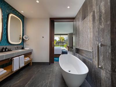 Moderne Hotellobby mit freistehender Badewanne, grauen Fliesen und Waschbecken mit beleuchteten Spiegeln.