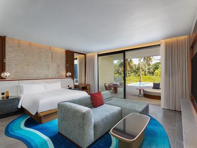 Modernes Hotelzimmer mit großer Glasschiebetür, Komfortbett, Sofa und Blick auf tropische Außenanlage.