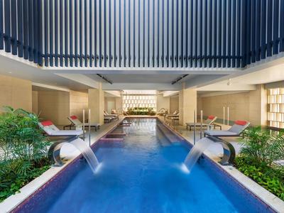 Moderner, überdachter Poolbereich mit Wasserfontänen, Liegestühlen und Pflanzen in einem Luxushotel.
