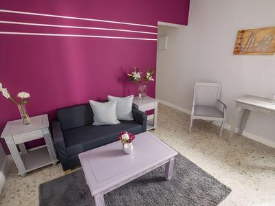 Soggiorno accogliente con parete viola, divano, tavolo e arredi chiari in camera d'hotel.