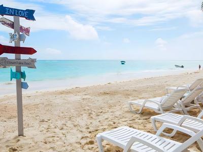 Spiaggia di sabbia bianca con sdraio e cartello multilingue vicino al mare azzurro.