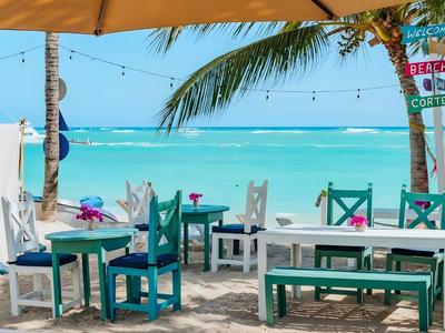 Ristorante sulla spiaggia all'aperto con mobili in legno colorati e vista sul mare turchese.