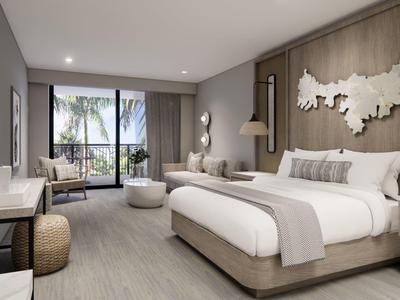 Nowoczesny pokój hotelowy z dużym łóżkiem, miejscem do siedzenia i balkonem z widokiem na palmy.