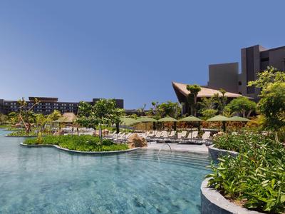 Piscina dell'hotel con acqua limpida, ombrelloni, aree relax e architettura moderna sullo sfondo.