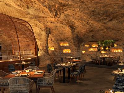 Útulná restaurace v jeskyni s teplým osvětlením a dekorativními svíčkami.