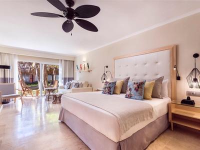 Camera luminosa con letto grande, ventilatore a soffitto e accesso al balcone con area salotto.