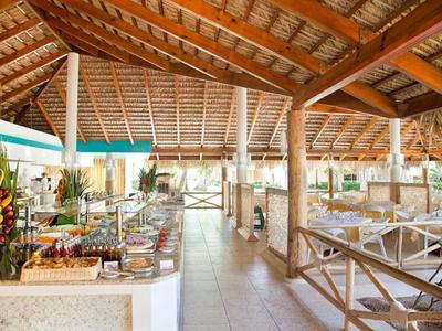 Area buffet aperta in resort tropicale con soffitto in legno e bambù e tavoli apparecchiati.