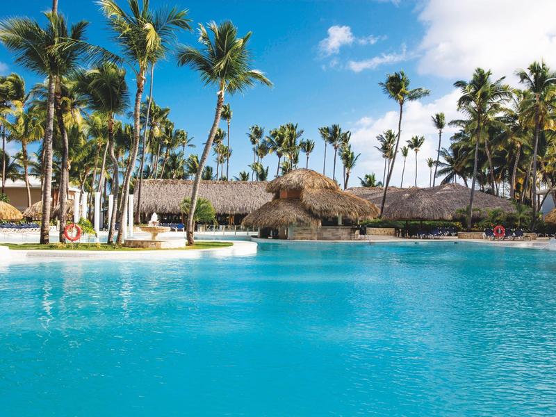 Grande piscina con acqua azzurra cristallina circondata da palme e diverse capanne con tetto di paglia.