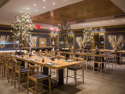 Moderní stylová restaurace s dlouhými dřevěnými stoly a dekorativními osvětlenými stromy.