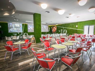 Světlá hotelová jídelna s červenými židlemi a zelenými stěnami.