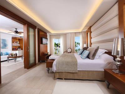 Moderní hotelový pokoj s velkou postelí, nepřímým osvětlením a výhledem na obývací část.