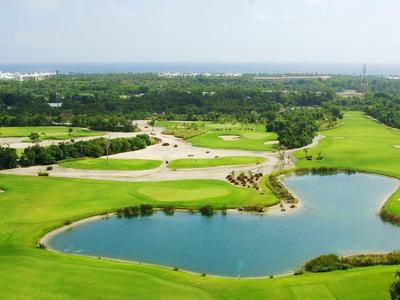 Zielone pole golfowe z jeziorem i widokiem na ocean w tle.