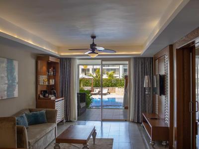 Obývací pokoj s výhledem na bazén přes velké posuvné dveře v moderním hotelovém pokoji.