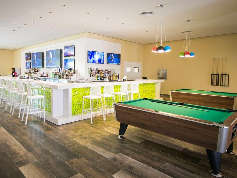 Moderní bar s bílými a zelenými stoličkami a dvěma kulečníkovými stoly v jasné místnosti.