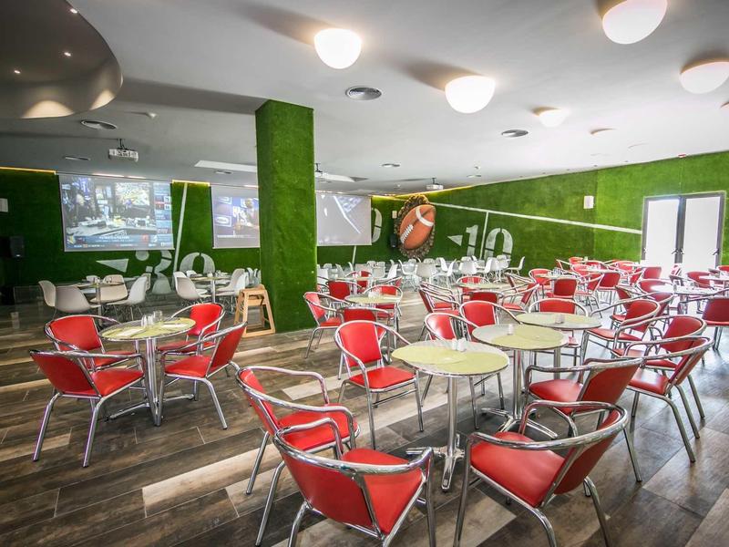 Světlá hotelová jídelna s červenými židlemi a zelenými stěnami.