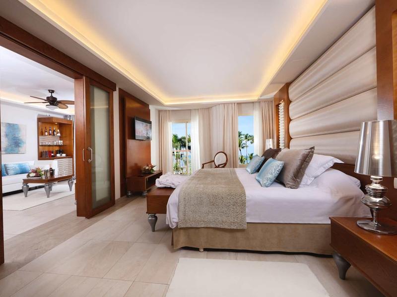 Moderní hotelový pokoj s velkou postelí, nepřímým osvětlením a výhledem na obývací část.