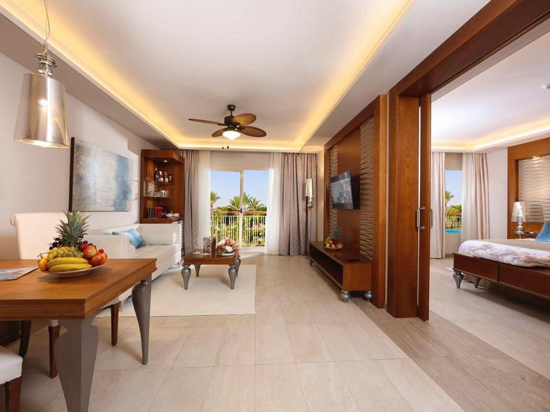 Světlá hotelová místnost s jídelním koutem, obývacím pokojem a ložnicí s přístupem na terasu.